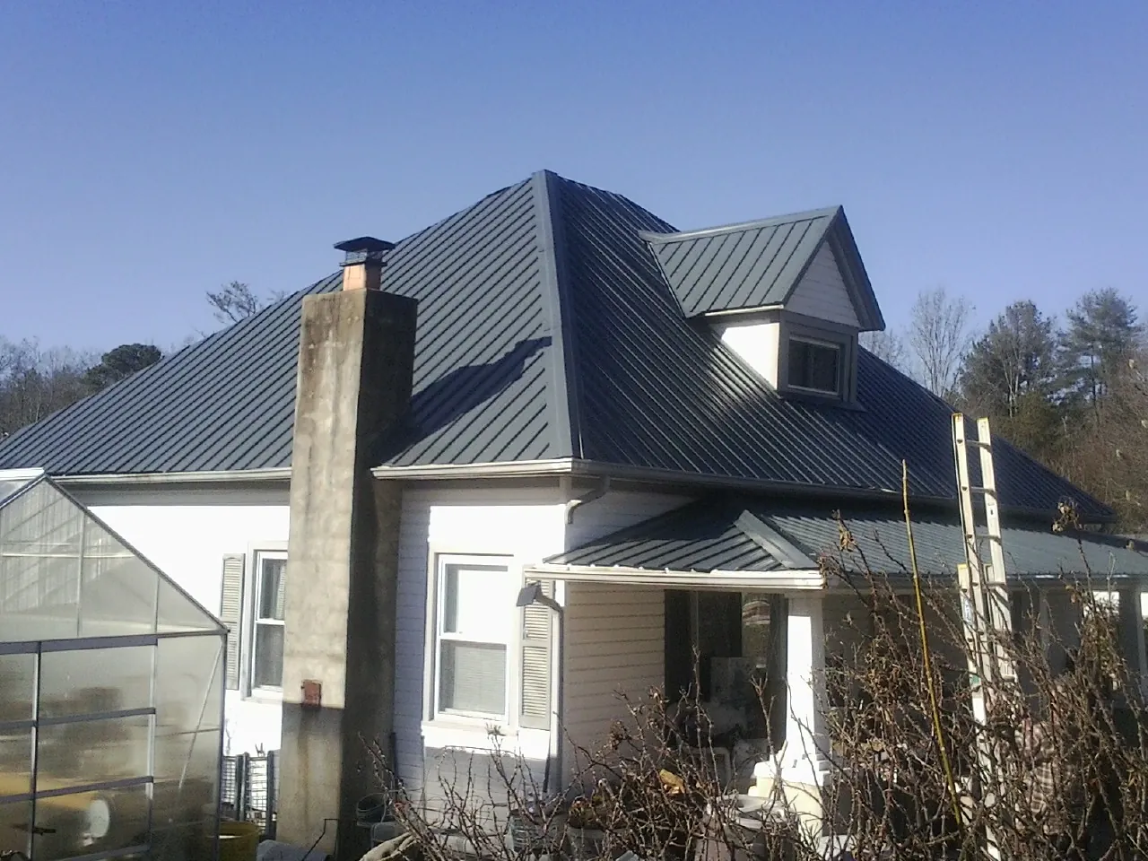 Dark blue standing seam metal roof on a white farmhouse with dormer — Slate & Tile Roof Repair by Roofing Brothers in North Clarendon