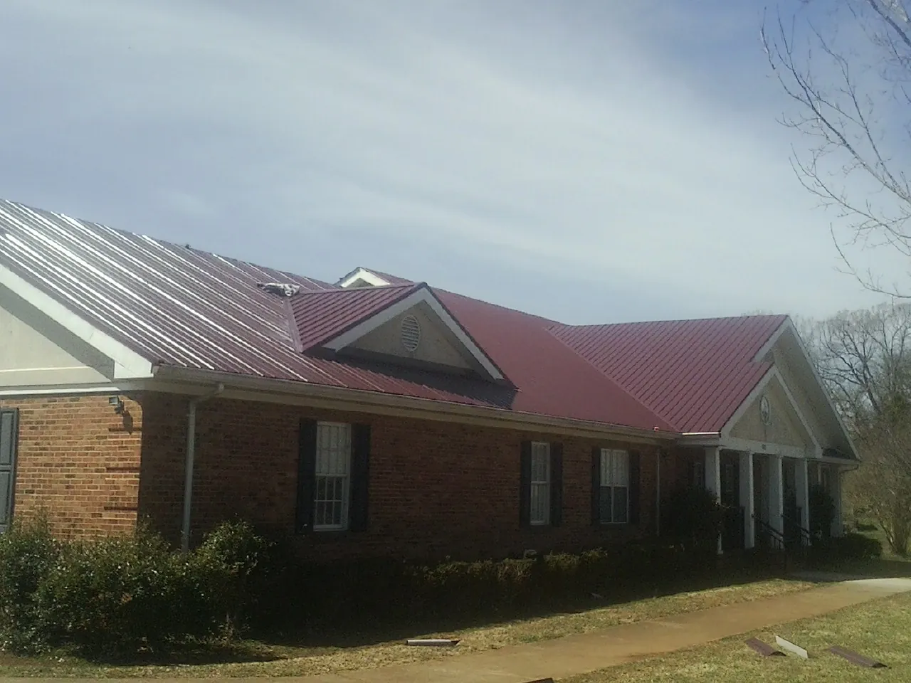 Red metal roof with gabled entries on a long brick building, from a Hail Damage Roof Repair job in North Clarendon