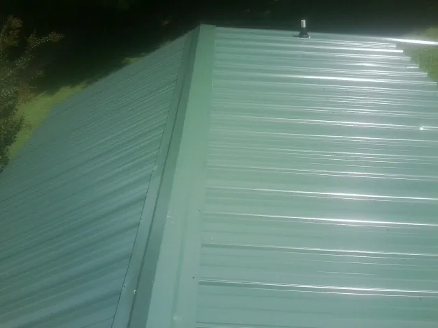 New green metal panels meeting at the ridge of a roof — Flat Roof Repair work by our crew in North Clarendon