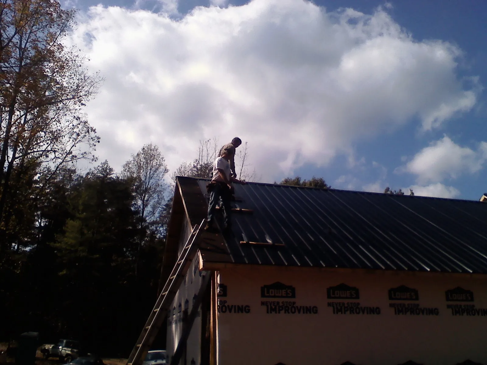 Roofer fastening dark metal panels high against a cloudy sky, from a Roof Inspection job in North Clarendon