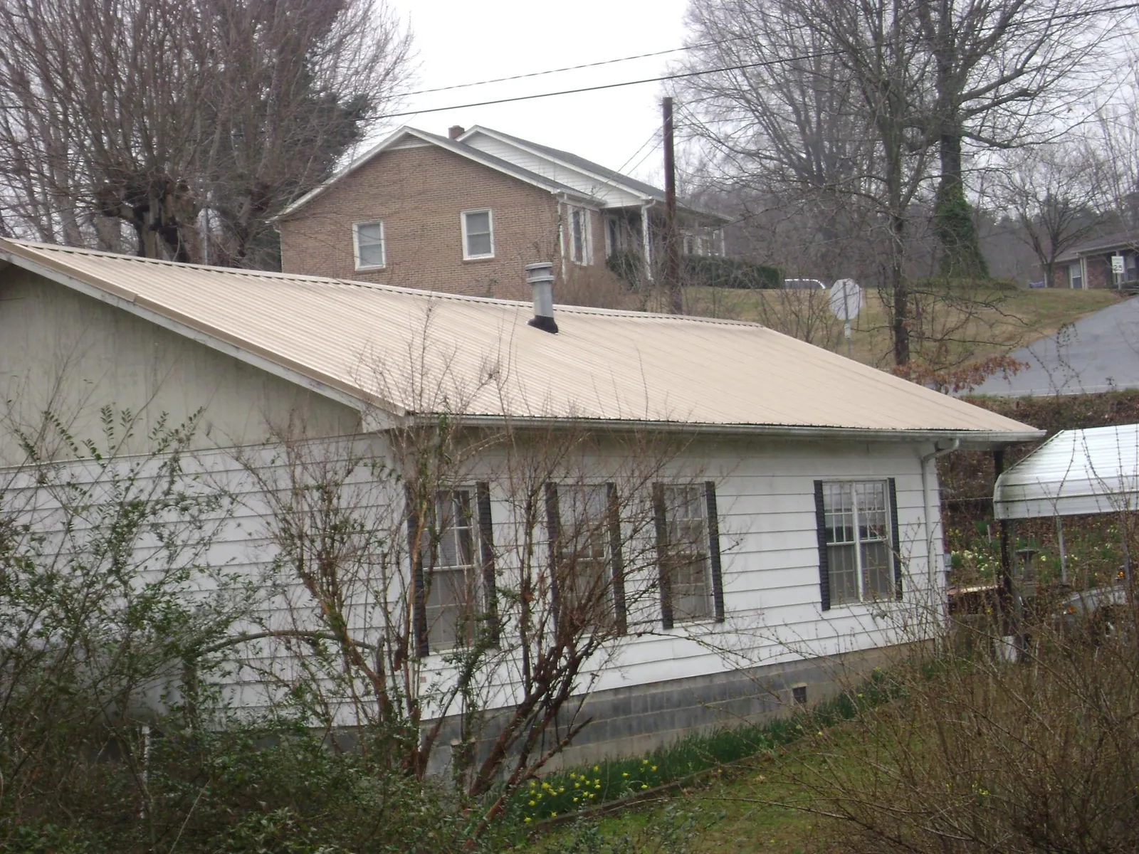 Tan metal roof on a white sided house set into a hillside — Commercial Roofing by Roofing Brothers in North Clarendon