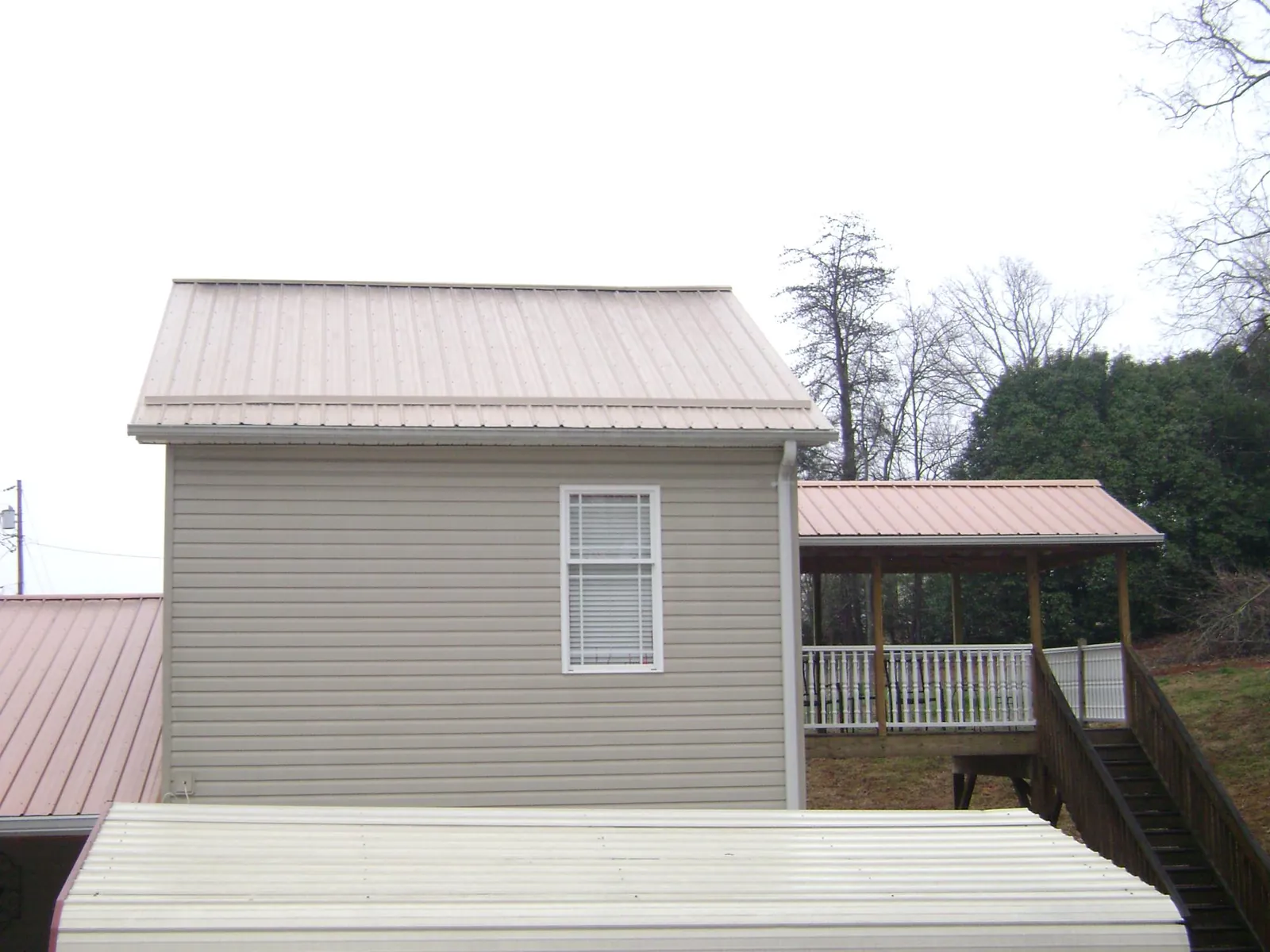 Tan metal roofs on a two story addition and attached porch, from a Roof Replacement job in North Clarendon